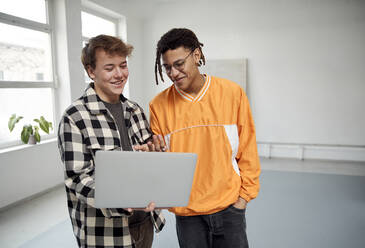 Smiling young man sharing laptop with friend - SUF00700