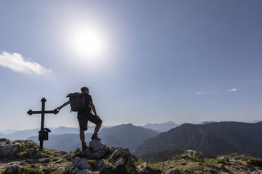 Deutschland, Bayern, Sonne scheint über die Silhouette eines männlichen Wanderers am Fockenstein-Gipfelkreuz - FOF13102