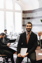 Porträt eines lächelnden männlichen Anwalts, der einen Laptop hält und auf einem Schreibtisch im Büro sitzt - MASF29285