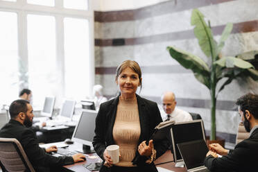 Portrait of smiling mature female leader holding coffee cup and documents at law office - MASF29287