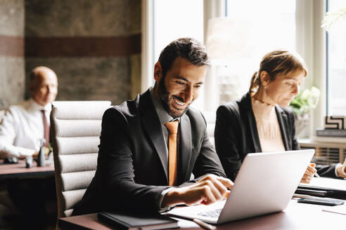 Smiling businessman using laptop working by businesswoman at desk in law office - MASF29350