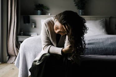 Emotional depressive Frau sitzt mit der Hand im Haar auf dem Bett zu Hause - MASF29438