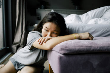 Thoughtful emotionally ill woman leaning on bench in bedroom at home - MASF29448