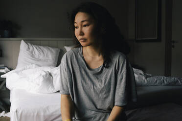Thoughtful lonely woman looking away sitting in bedroom at home - MASF29453