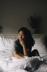 Thoughtful mentally depressed woman looking away while sitting on bed at home - MASF29456