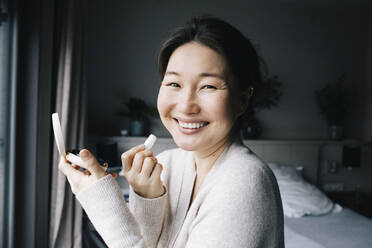 Portrait of happy woman applying make-up in bedroom at home - MASF29464
