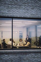 Geschäftsfrau diskutiert mit männlichen und weiblichen Kollegen durch das Fenster eines Büros gesehen - MASF29514