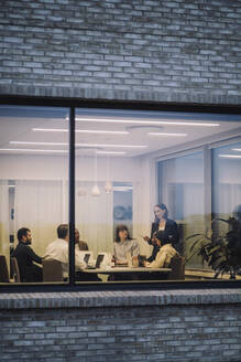 Businesswoman discussing with male and female colleagues seen through window of office - MASF29514
