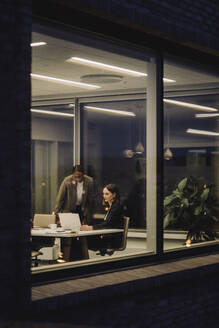 Mature businesswoman discussing with female colleague in office at night - MASF29529