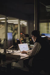 Businesswoman using laptop while working overtime in office at night - MASF29534