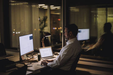 Businessman typing on computer keyboard while working in office at night - MASF29538