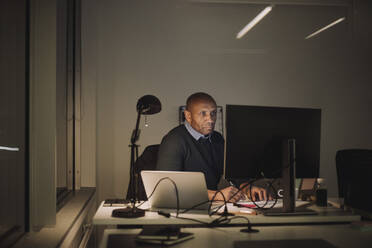 Dedicated businessman using computer while working overtime in office at night - MASF29557