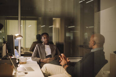 Mature businessman planning strategy with female colleague seen through glass of office - MASF29562