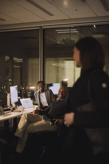 Happy female and male colleagues discussing with businesswoman at work place - MASF29566