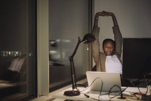 Tired businesswoman stretching hands while working in office at night - MASF29575