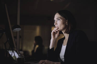 Mature businesswoman with hand on chin working over computer at work place - MASF29578