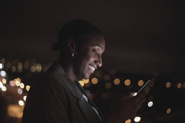 Smiling businesswoman text messaging on mobile phone at night - MASF29616