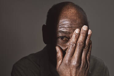 Älterer Mann bedeckt Auge mit Hand im Studio - MASF29639