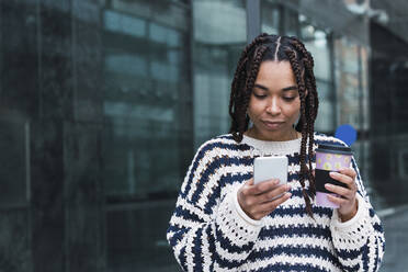 Young businesswoman with disposable coffee cup using mobile phone at office park - PNAF03604