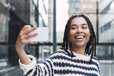 Happy young businesswoman taking selfie through mobile phone at office park - PNAF03606