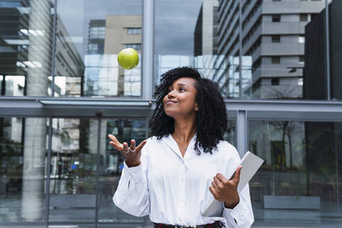 Lächelnde Geschäftsfrau, die einen Apfel im Büropark fängt - PNAF03630
