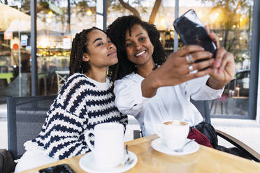 Smiling colleagues taking selfie through smart phone at sidewalk cafe - PNAF03651