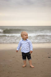 Smiling cute boy standing at beach - SSGF00635