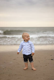 Lächelnder süßer Junge am Strand stehend - SSGF00635