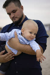 Father carrying son on beach at sunset - SSGF00638