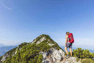 Frau mit Rucksack schaut auf einen Berg an einem sonnigen Tag - FOF13111