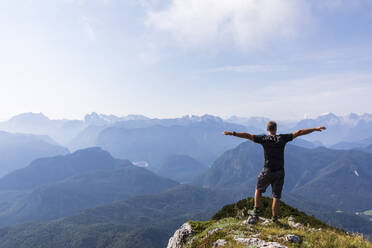 Mann steht mit ausgestreckten Armen auf einem Berggipfel an einem sonnigen Tag - FOF13115