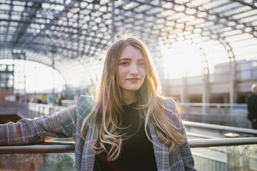 Junge Frau mit blondem Haar steht am Geländer - FBAF01987