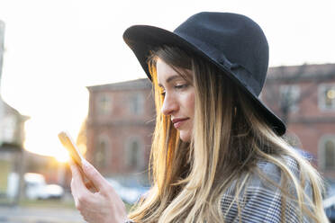 Young woman with blond hair wearing hat using smart phone - FBAF01989