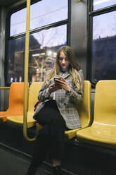 Junge Frau mit Mobiltelefon in der Straßenbahn sitzend - FBAF01990