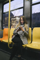 Young woman using mobile phone sitting in tram - FBAF01990