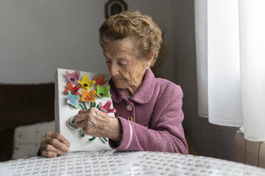Ältere Frau, die am Esstisch sitzend Papierarbeiten dekoriert - JCCMF06021