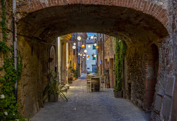 Italien, Provinz Siena, Radicondoli, Laternen beleuchten Altstadtgasse mit Backsteinbogen im Vordergrund - MAMF02123