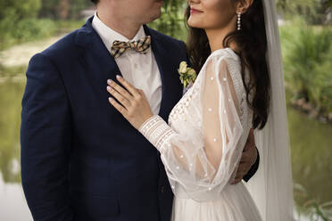 Smiling bride embracing groom standing with arm around - SSGF00663