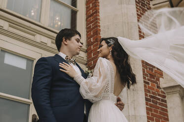 Smiling bride embracing groom in front of building - SSGF00669