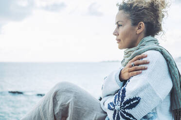 Nachdenkliche Frau in warmer Kleidung, die sich am Meer umarmt - SIPF02840