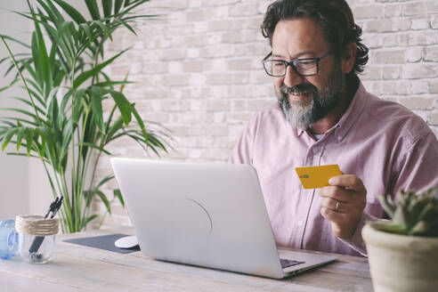 Lächelnder Geschäftsmann mit Kreditkarte beim Online-Shopping mit dem Laptop zu Hause - SIPF02848