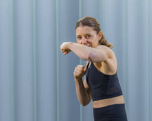 Smiling woman practicing boxing in front of wall - STSF03167