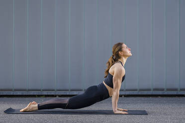 Woman practicing cobra pose in front of wall - STSF03170