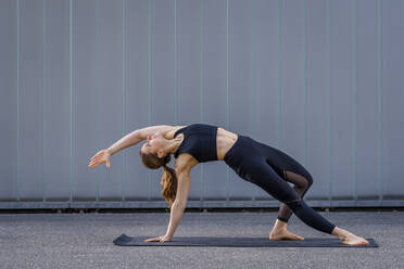 Woman practicing yoga on footpath by wall - STSF03171