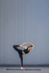 Athlete in sportswear doing yoga on footpath in front of wall - STSF03173