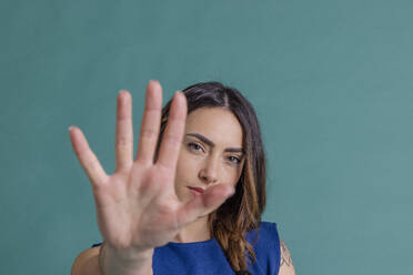 Junge Frau gestikuliert Stopp mit der Hand vor blauem Hintergrund - EIF03824