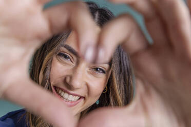 Cheerful young woman making heart shape in front of face - EIF03826
