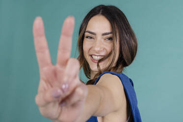 Lächelnde Frau gestikuliert Friedenszeichen vor blauem Hintergrund - EIF03876
