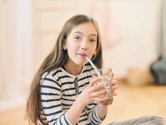 Mädchen trinkt ein Glas Wasser auf dem Boden sitzend zu Hause - DIKF00675