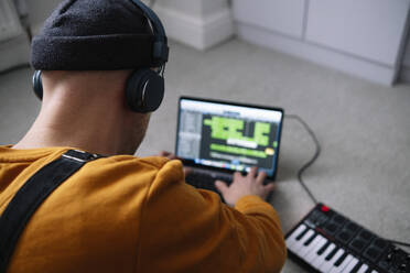 Freiberufler mit drahtlosen Kopfhörern, der einen Laptop am Klavier im Heimstudio benutzt - ASGF02255